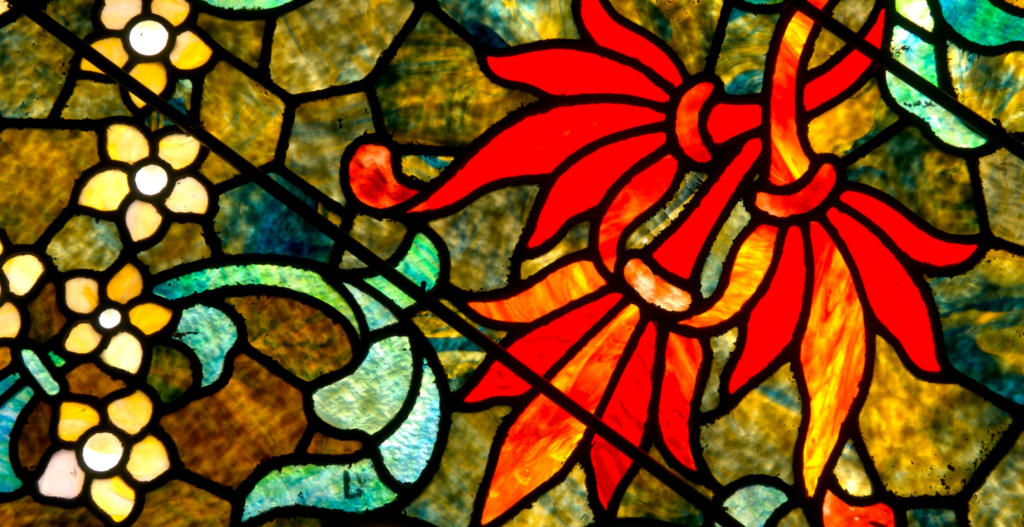 close up of floral stained glass window with bold red flower and yellow blossoms on a golden green background