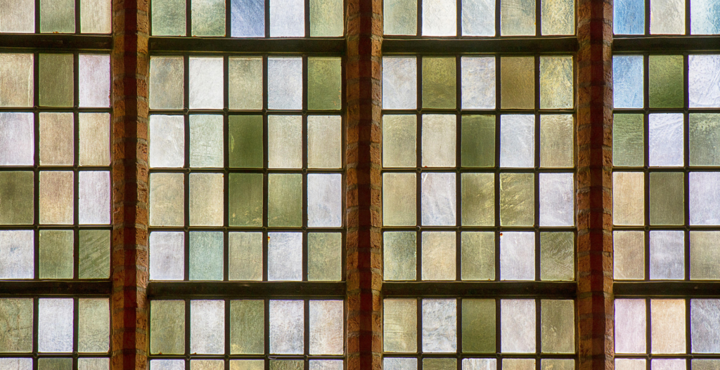 large grid of antique stained glass window panes in soft green grey and white tones set in warm brick and lead framing in an arts and crafts style
