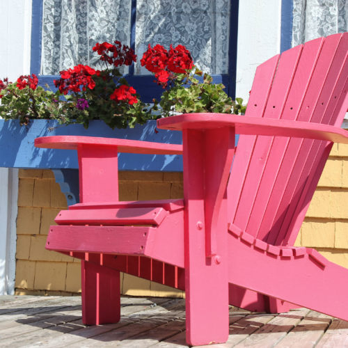 Front porch decor with a red Adirondack chair, red flowers, and plant pots creating a welcoming entry