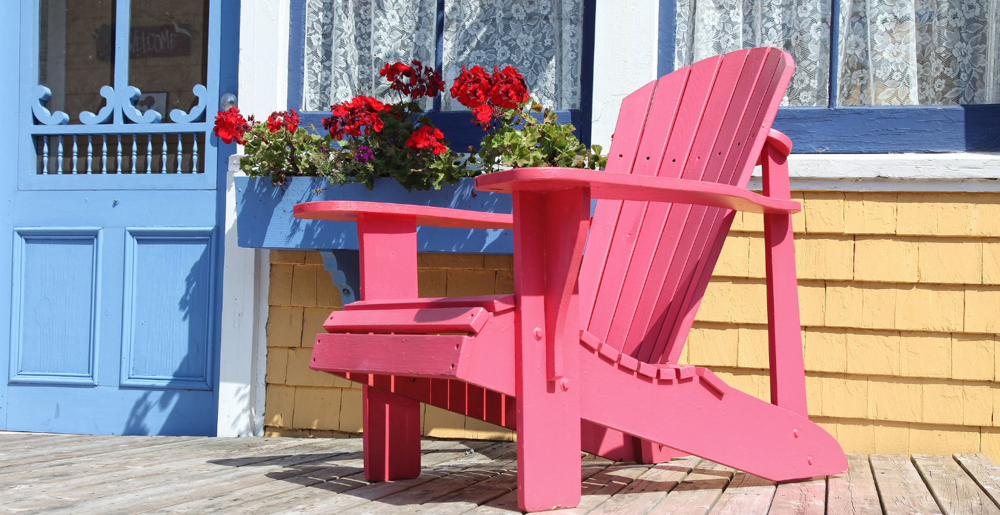 Front porch decor with a red Adirondack chair, red flowers, and plant pots creating a welcoming entry